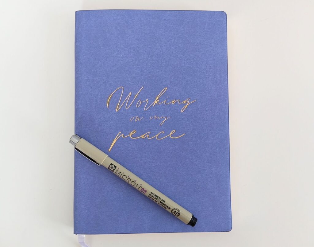 Purple notebook with gold text and a pen on a white background
