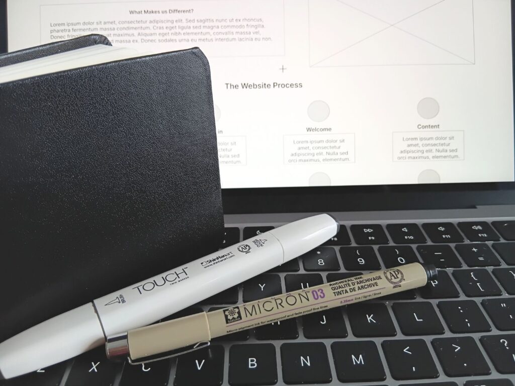 Notebook and pens on laptop keyboard with website planning on screen